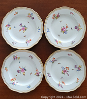 Four plates top view showing floral and insect motifs and scalloped gold rims