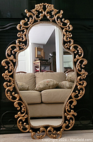 Full view of ornate decorative gilt metal framed mirror against black screen with sofa reflected.