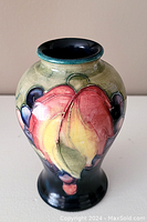 Front view showing colorful floral pattern on vase with green background and dark base.