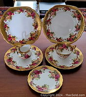 Full view of all china pieces arranged on table showing golden scalloped edges and rose pattern