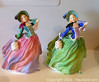 Pair of Royal Doulton figurines on display, showing both pink and green dresses