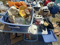 Bin containing assorted decorative and dish items including a yellow ceramic shell dish, black ceramic elephant, glassware, and red ornaments