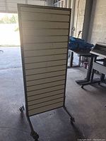 Full view of the freestanding merchandise slatwall display board showing horizontal slats and caster wheels.