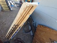 Three plywood sheets stacked and leaning against a support outdoors on gravel ground