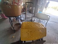 Photo showing two champagne buckets on black metal pedestals and a yellow metal decorative piece with cut-out designs placed on the ground.