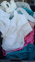Photo showing various folded and crumpled curtain and linen fabrics in assorted colors including white, teal, pink, and cream.