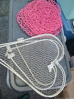 Close-up of pink woven heart and white metal mesh heart decorations placed on a table.