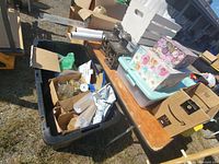 Bin with assorted glassware and boxes on table outdoors, among other items