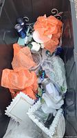 Overhead view of contents inside a storage bin showing blue glass jars, white dishes, artificial flowers, and wrapped items.