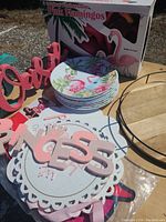 Lot contents including stacked flamingo plates, boxed pink flamingo lawn ornaments, and several pink and white wooden word signs.