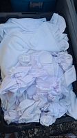 Photo showing a bin filled with multiple white linens such as sheets and pillowcases, some tags visible.