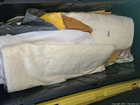 Top view of linen tableskirts and fabric rolls in a black storage container, showing cream, white, and mustard colors.