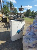 White mini fridge outdoors with electrical cord and several tiered metal cupcake stands placed on top.