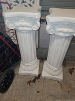 Two white decorative pedestals placed side by side, displaying their fluted columns and ornate capitals.