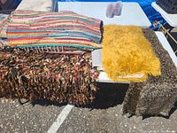 Photo of assorted rugs stacked on a table showing colorful striped, shaggy multicolor, yellow shaggy, and two animal print rugs.