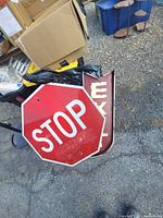 Photo showing a red octagonal STOP sign and a red rectangular EXIT sign with faded paint, placed on the ground near some boxes and blue containers.