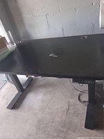Black topped 6 ft electric height adjustable desk showing wear and chipped area on surface.