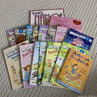Photo showing all Fancy Nancy and Amelia Bedelia books in the lot laid out on a carpeted floor, bright covers visible with titles.