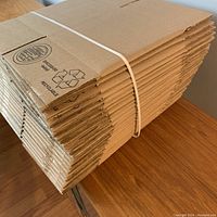 Stack of flattened 6x6x6 cardboard boxes bound with a white plastic strap, showing the thickness and quality of the cardboard.
