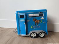 Blue Breyer two-horse show trailer model front side view showing door, horse graphics, and wheels.