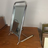 Full view of the floor mirror with chrome frame and stand placed on wooden surface