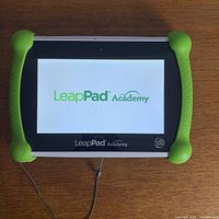 Front view of LeapPad Academy tablet displaying the logo on screen, showing its green rubber corner bumpers and screen size.