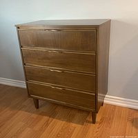 Front-side view of the dresser showing the four drawers with integrated handles and tapered legs, highlighting the wood grain and finish.