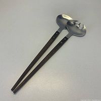 Two mid-century salad serving utensils laid on a white surface, showing stainless steel heads and dark wooden handles.