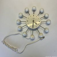 Full front view of white atomic ball clock with cord and plug visible