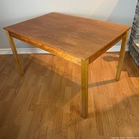 Front angle view of the mid century wood dining table showing its square post legs and wood grain top.