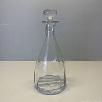 Full view of the clear glass wine decanter with stopper on a white surface and neutral background.