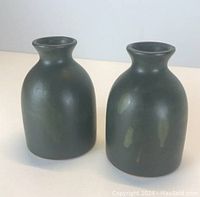 Side view of two small green pottery bud vases with a rounded body and narrow neck.