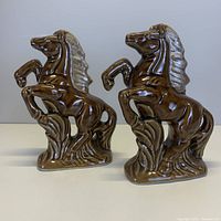 Front angle photo of both matching rearing horse bookends showing glossy brown glazed finish and detailed features on the horses and bases.