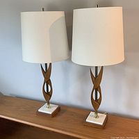 Pair of vintage mid century lamps on a wooden surface, showing wood twist design with white shades and stone bases.