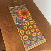 Full view of peacock yarn wall hanging showing colors, texture, and hanging loop.