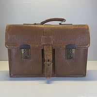 Front view of brown textured leather vintage briefcase with two front pockets, metal snap closures, central leather strap and handle.