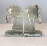 Front view of the two carved marble horse head bookends shown side by side, displaying their translucent layered stone and carved details.