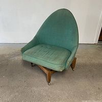 Front angled view showing the green fabric upholstery on a mid century swivel chair with visible wear and wooden caster base.