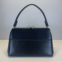 Front view of vintage black leather top handle handbag with perforated detail on pocket.