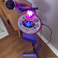 Close-up image of Vtech Kidi Super Star karaoke machine showing the microphone, disco ball light, control buttons and small display screen while in use.