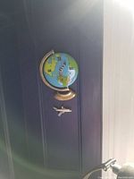 Photo of a globe-shaped novelty wall clock with an airplane figure underneath on a black vertical surface.
