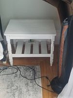 Front angle showing the bedside table with a flat top and slatted shelf below with some items on the shelf. Visible wear marks on the top surface.