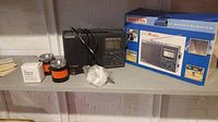 Sangean CC radio, original blue box, flashlight, power adapter, and a box of components displayed on a shelf