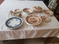 Overview of the china set on a white table cloth, showing grouped plates, bowls, cups, and a covered serving dish.