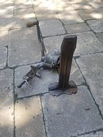 Close-up photo of the metal cobblers stand missing the foot base, placed on stone pavement.