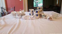 Wide view of collection of cups, saucers, creamers, and sugar bowl on table showing overall lot