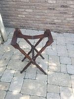 Folding wooden luggage rack standing open on stone tile ground, showing its structure and how it folds.