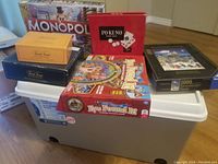 Various boxed games including Monopoly, Pokeno, Eye Found It, Trivial Pursuit, and Ravensburger puzzle