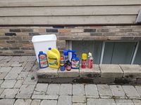 View of assorted car care and garden maintenance items placed on a stone ledge in front of a brick wall.