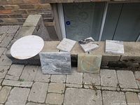 All marble pieces arranged on a stone ledge including one round and several square pieces in various colors.